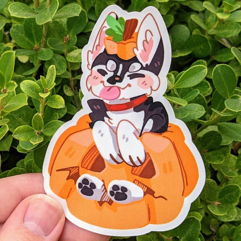 Hand holding Halloween Puppies Stickers featuring a cartoon dog sitting in a pumpkin with greenery in the background.