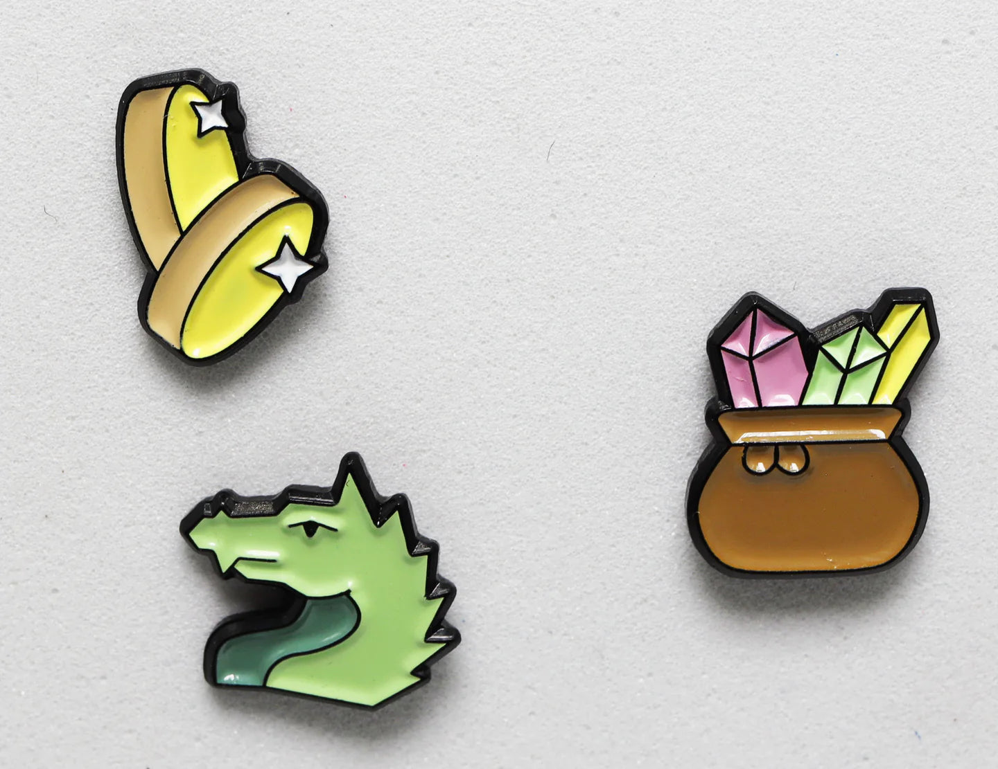 Dragons Hoard Mini Pins Pack: three metal pins featuring bananas with stars, a green dragon, and a crystal pot.