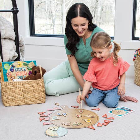 Woman and girl playing Snack Party Pals preschool board game for fine motor skills on a carpet.