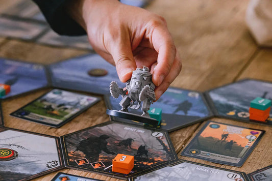 Scythe Expeditions Ironclad edition with a hand moving a robot game piece, cards, and cubes on a hexagonal board.