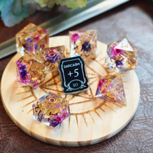 Floral resin dice set and Sarcasm +5 Stat acrylic pin displayed together.