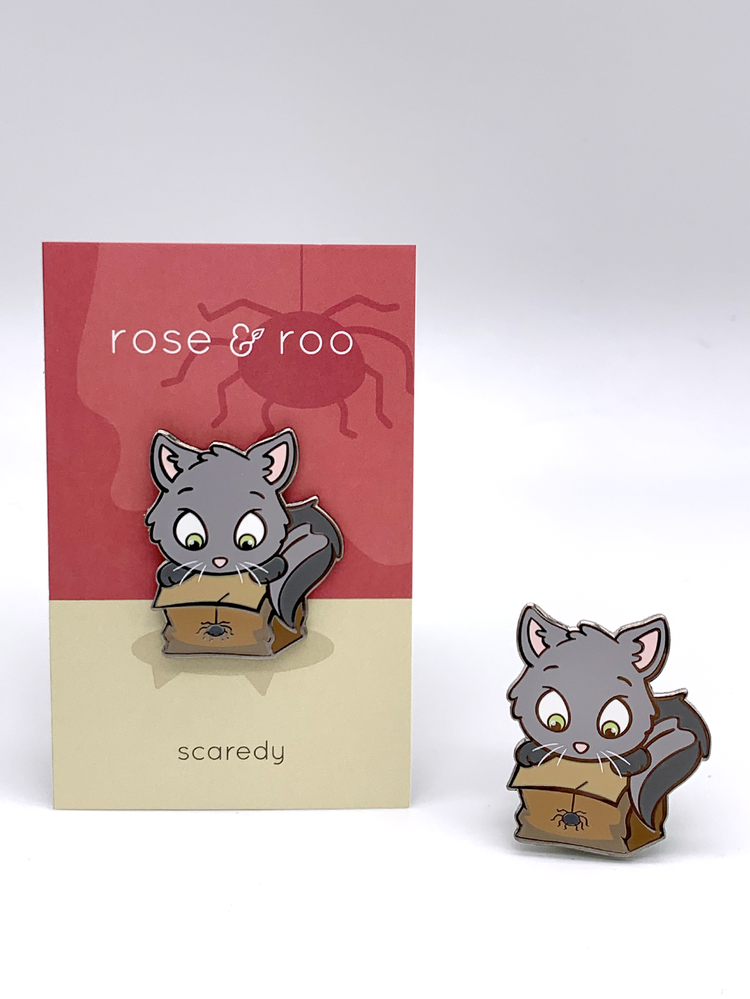 Scaredy Enamel Pin by rose & roo showing a gray cartoon cat with wide eyes looking into a paper bag with a spider.