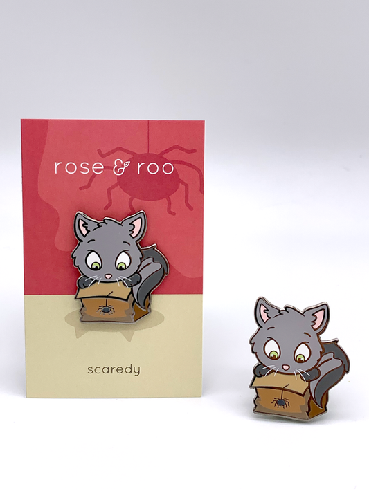 Scaredy Enamel Pin by rose & roo showing a gray cartoon cat with wide eyes looking into a paper bag with a spider.