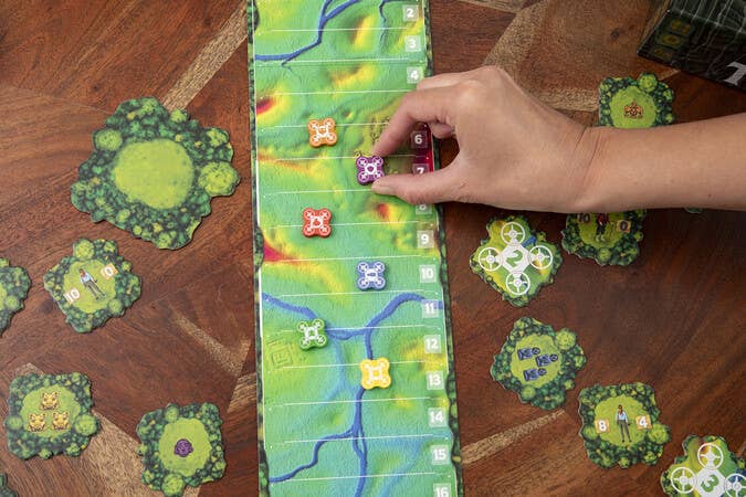 Trail To The Temple board game with a hand moving a purple token; other tokens and cards are nearby.