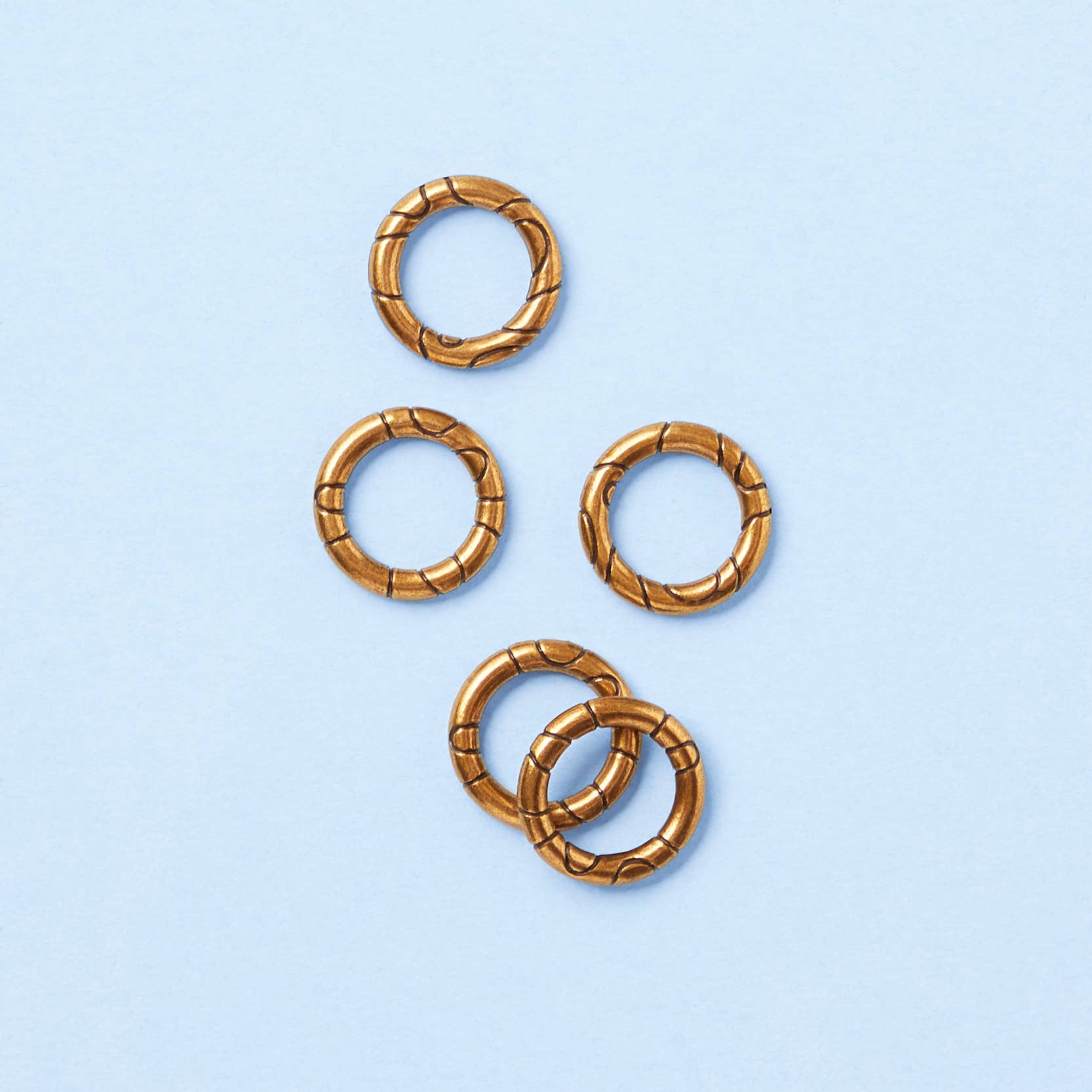Five textured gold rings on a light blue background, inspired by the Karmaka card game.
