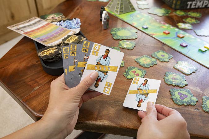 Trail To The Temple adventure board game cards and pieces held and arranged on a wooden table.