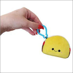 Micro Taco plush keychain shaped like a smiling yellow taco with a blue clip, held in a hand.