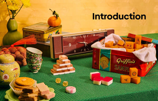 Mahjong set with assorted snacks, tea cups, retro clock, dice, and strategy guide on green tablecloth.