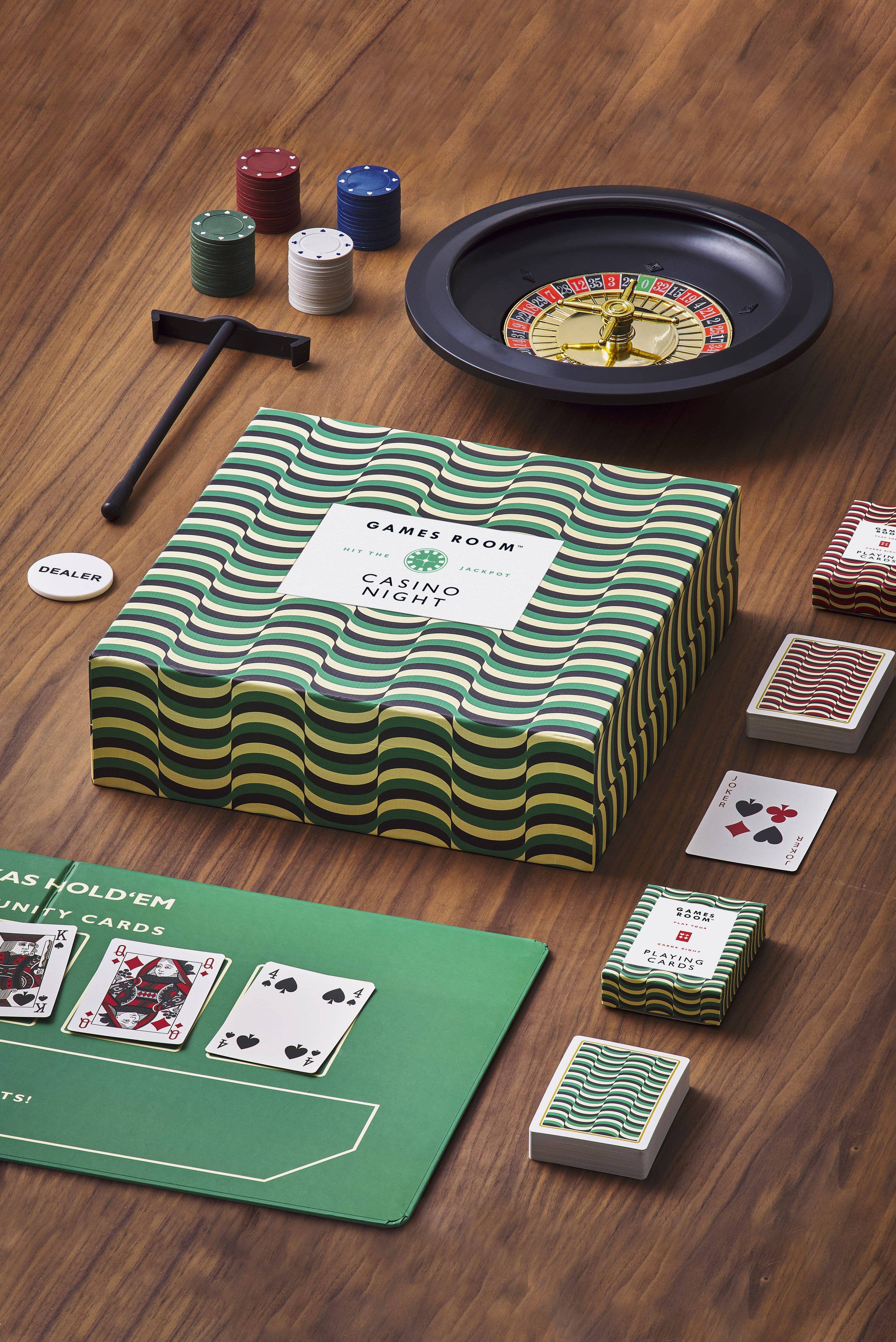 Casino Night set including cards, poker chips, roulette wheel, and green felt mat on a wooden table.