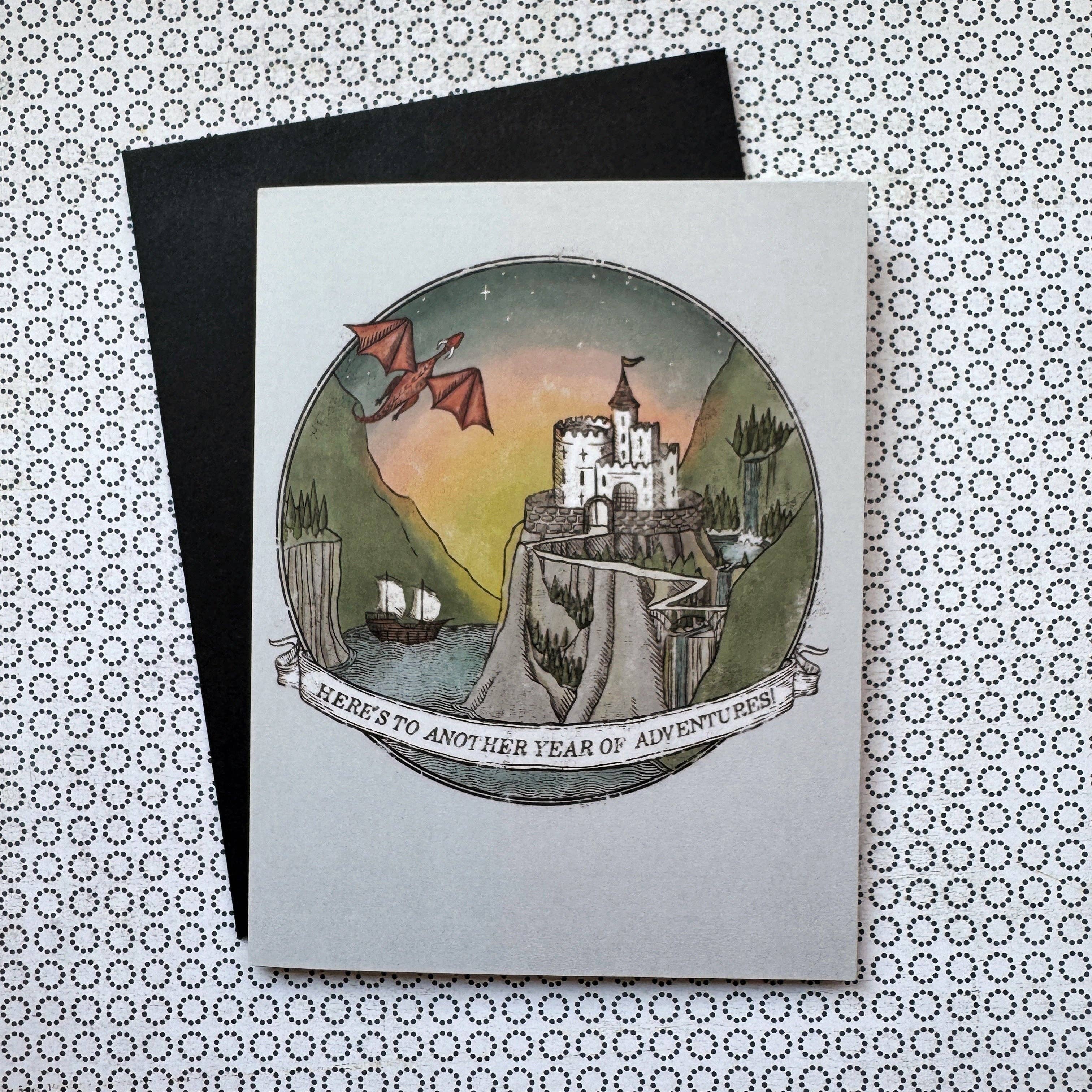 A5 fantasy birthday card with Heres to Another Year of Adventure text, castle, dragon, ships design; blank inside.