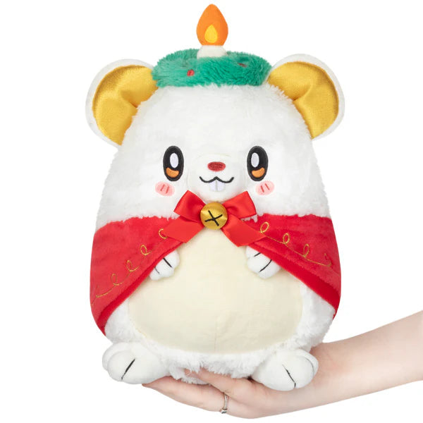 Festive Mouse Mini Squishable plush with red cape, bow, and flame-topped green hat, shown held in a hand.
