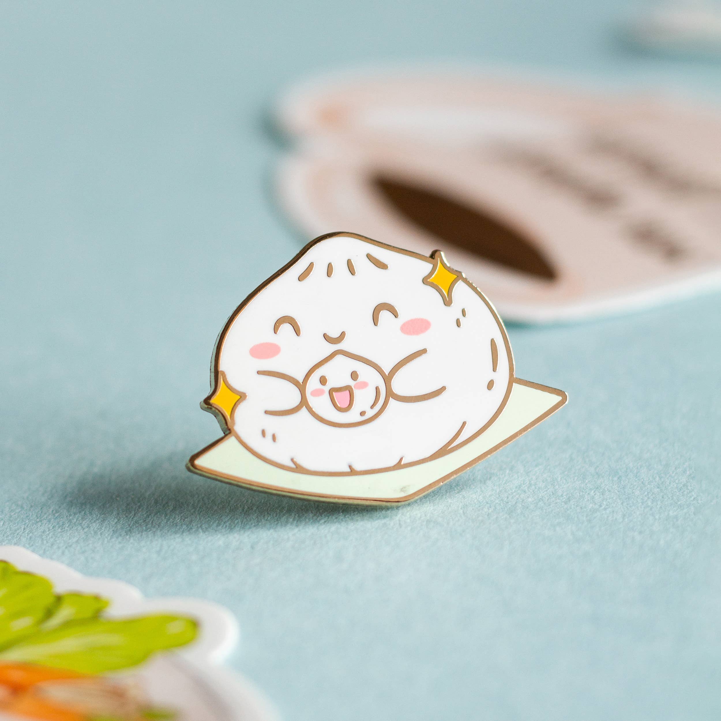 The Big and Little Baos enamel pin featuring smiling dumplings with sparkles on a light blue background.