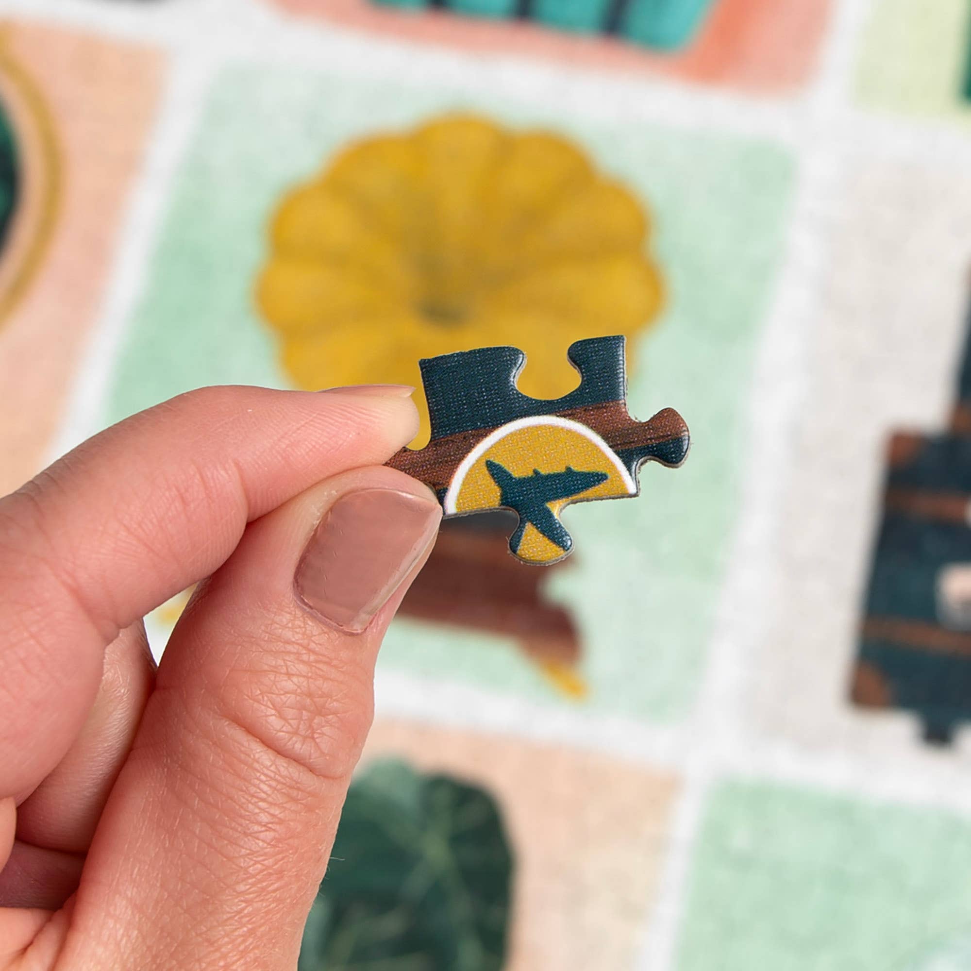 Hand holding a Simple Joys Puzzle piece featuring an airplane and yellow sun design.