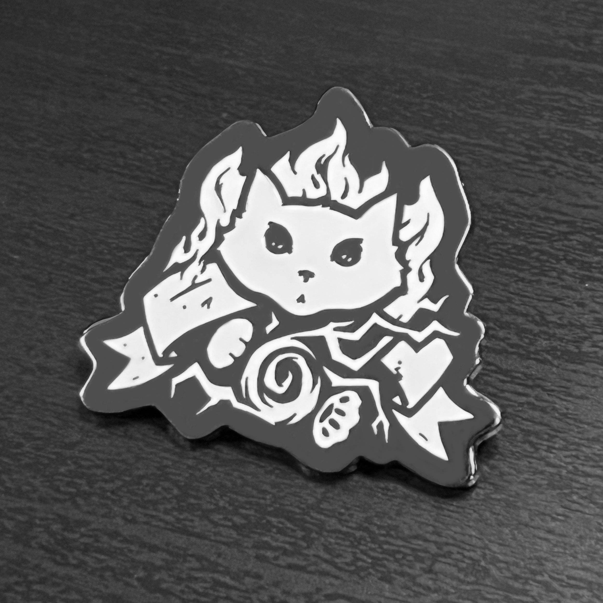 Enamel pin of a cat in wizard robes, casting a spell with a staff, in black and white enamel.