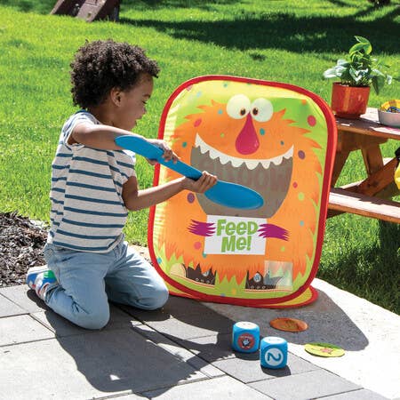 Child kneels outdoors, using a blue scoop to play the Giant Feed The Woozle game.