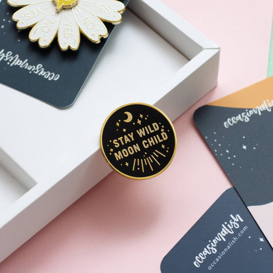 Stay Wild Moon Child enamel pin in black and gold with stars and moons design.