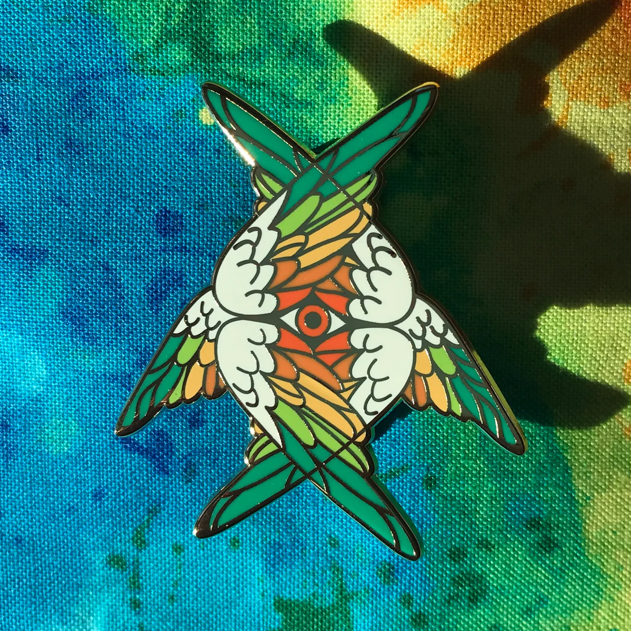 Heart Seraphim Pin with mirrored, intertwined birds on a blue and yellow tie-dye background.