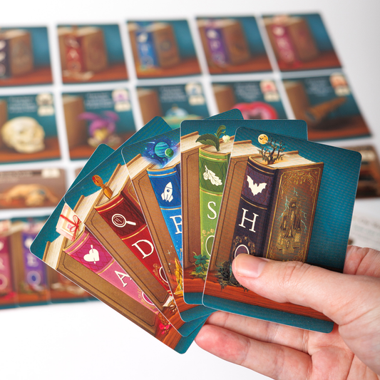 Hand holding colorful My Book Nook word game cards, with the themed game board in the background.