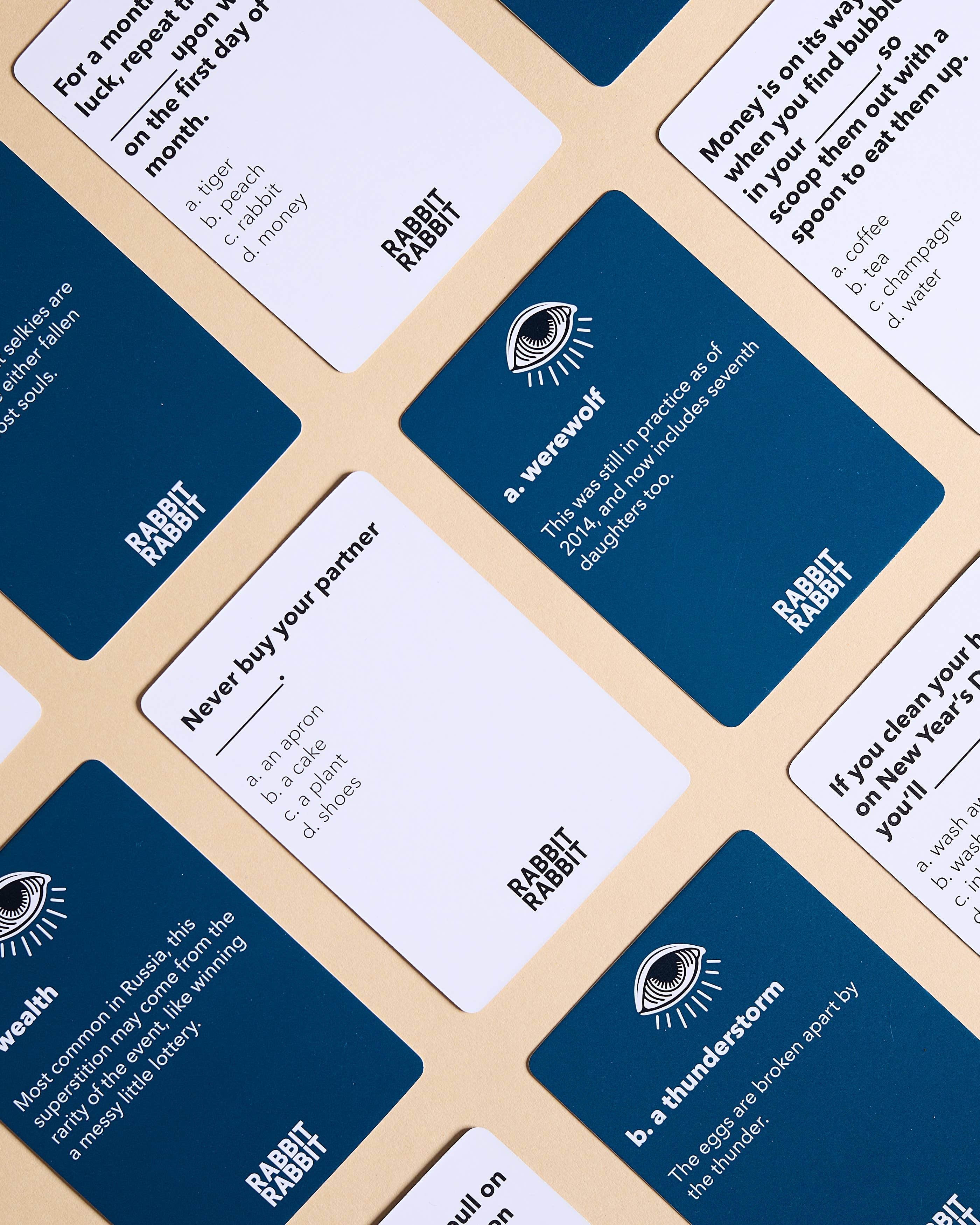 Rabbit Rabbit: A Game of Superstitions blue and white cards arranged on a beige surface.