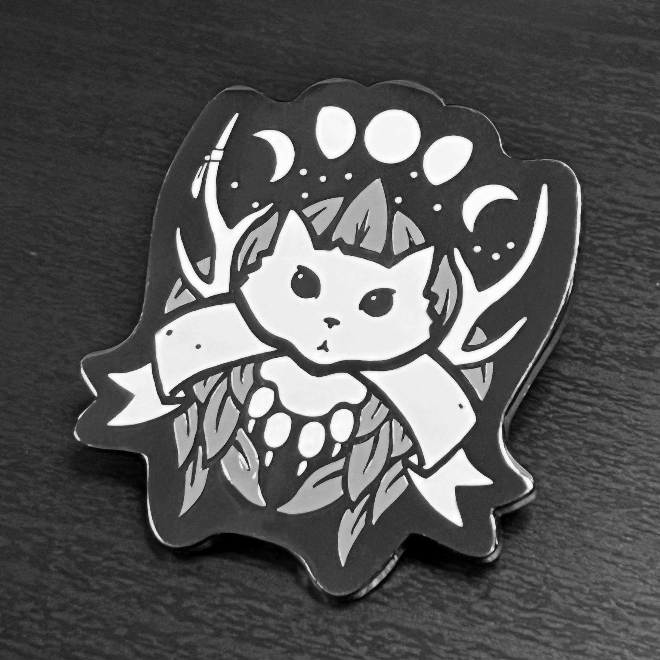 Druid enamel pin featuring a black and white cat with antlers, blank banner, moons, and leaves on black nickel plating.