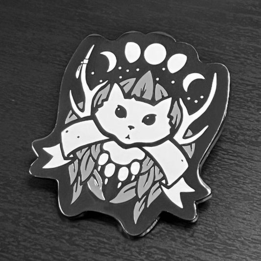 Druid enamel pin featuring a black and white cat with antlers, blank banner, moons, and leaves on black nickel plating.