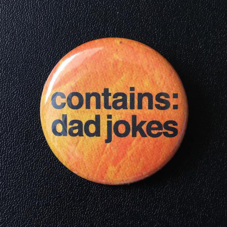 Contains Dad Jokes button pin, round orange with black text, on a black textured background.