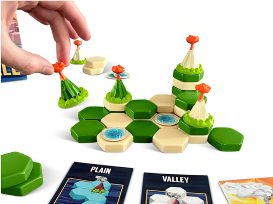 Hand placing volcano piece on hex tile board from Landfall: Base Game, a 3D strategy game with lakes and terrain cards.