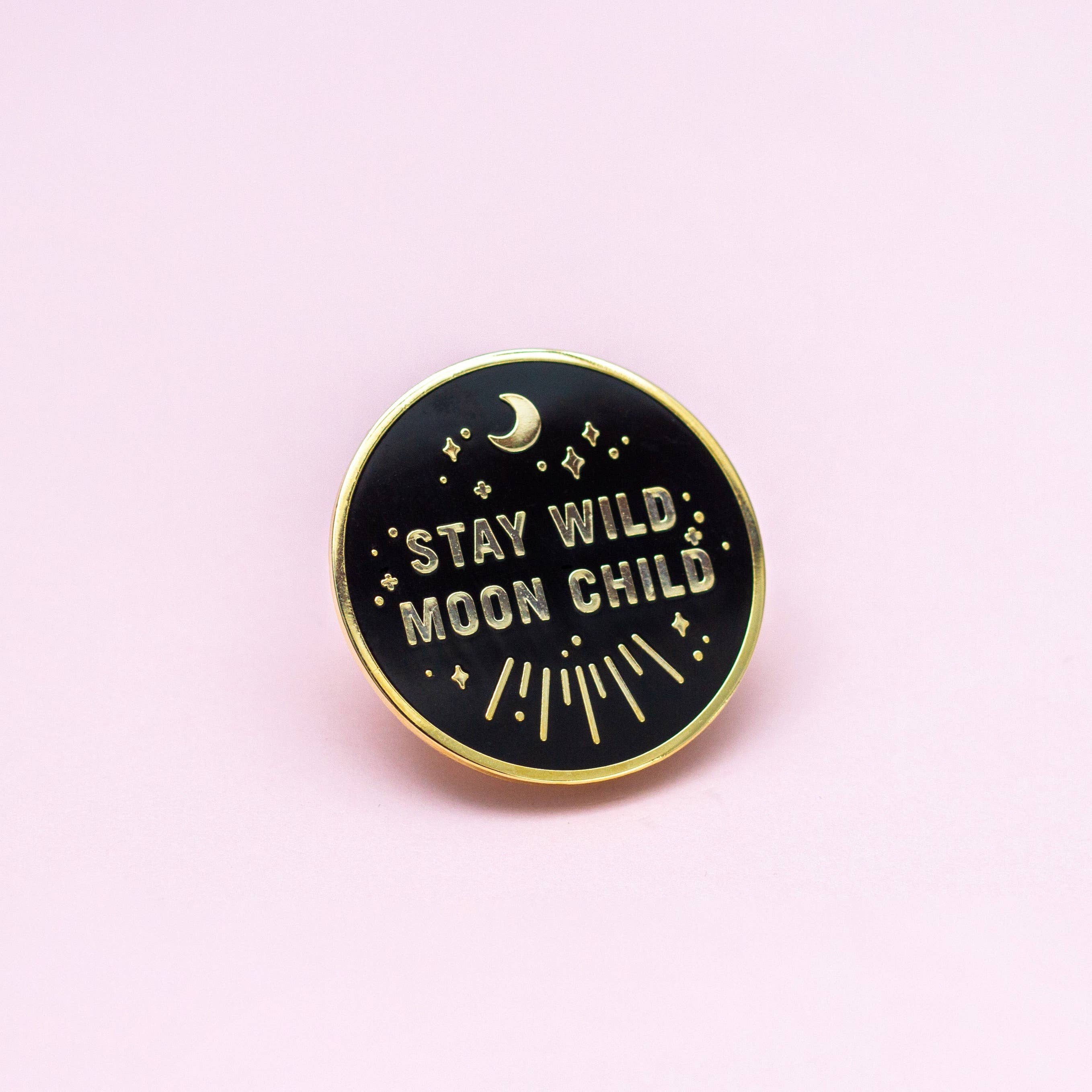 Stay Wild Moon Child enamel pin, round black hard enamel with gold trim, stars, crescent moon, and pink background.