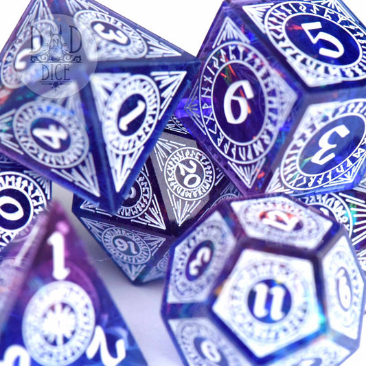 Helheim Hold handmade 7-dice set in purple-blue resin with white numbers and detailed tabletop designs.