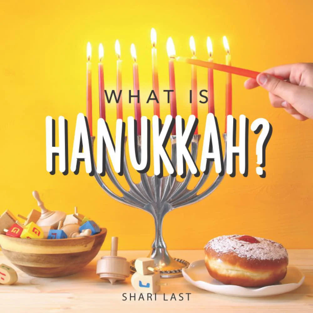 What is Hanukkah? Kids Book displayed with a menorah, dreidels, and a donut; hand lighting the menorah.