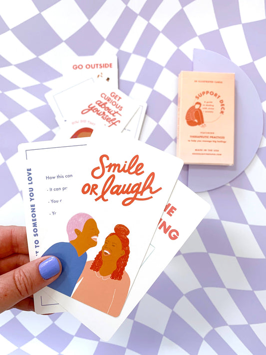 Hand holding a Support Deck - Mental Health Card with two people laughing and the word Smile or Laugh.