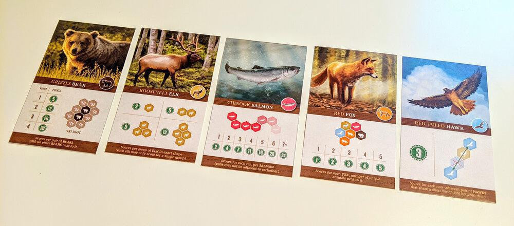 Cascadia board game wildlife cards set: bear, elk, salmon, fox, and hawk with stats displayed.