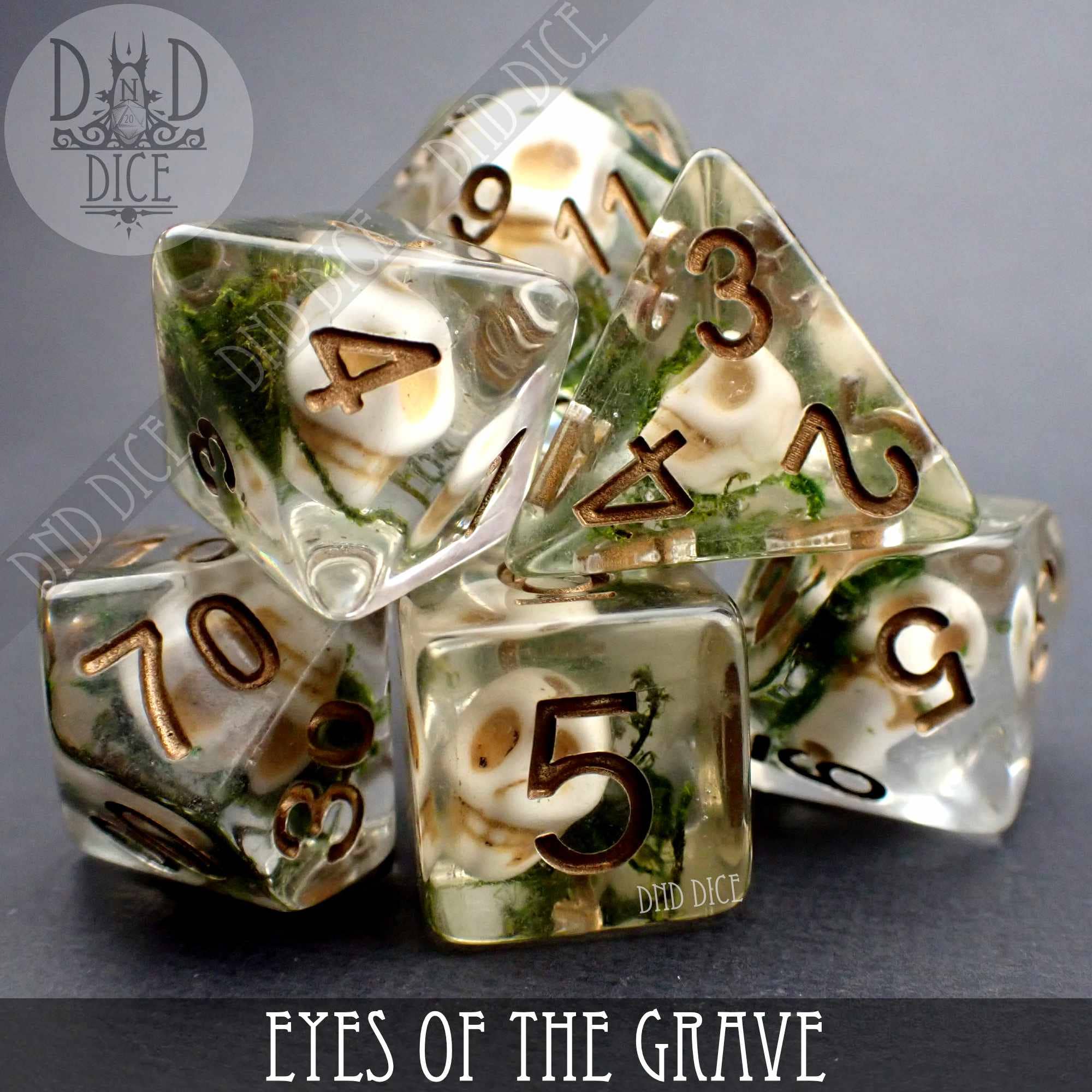Eyes of the Grave 7-piece clear resin DnD dice set with miniature skulls and moss inside.