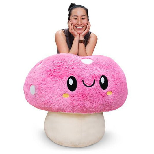 Massive Mushroom large pink plush with a smiling face, shown with a woman leaning on it.