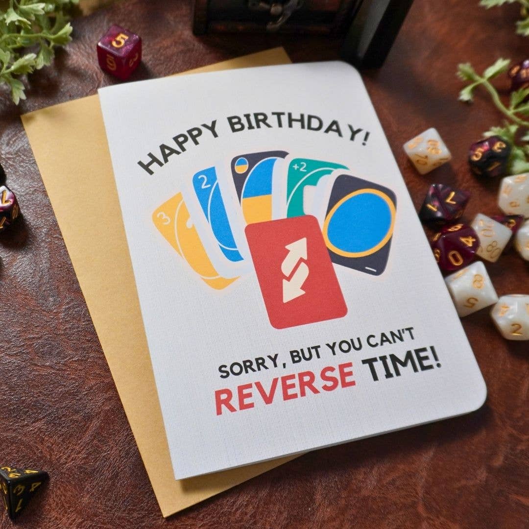 UNO Birthday Card with HAPPY BIRTHDAY SORRY, BUT YOU CANT REVERSE TIME and dice on a leather table.