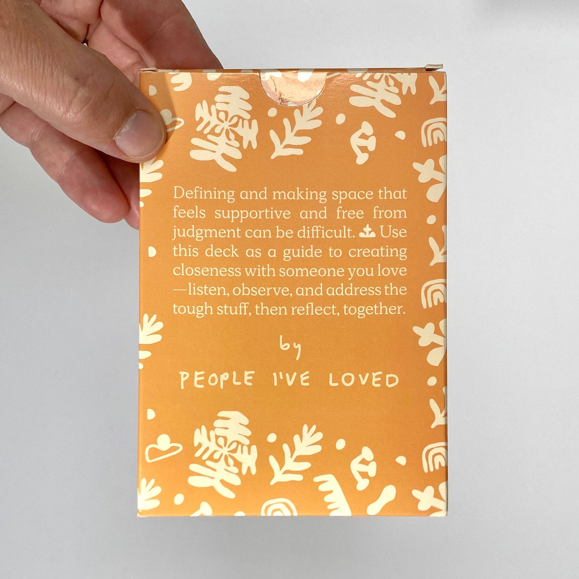 A Safe Space For Us Deck, orange box with white illustrations and prompts for couples, held in one hand.