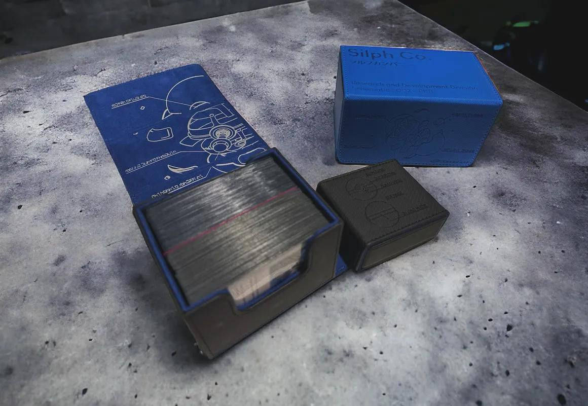 Box of trading cards, blue diagram mat, and Cardware Deckbox on a speckled surface.