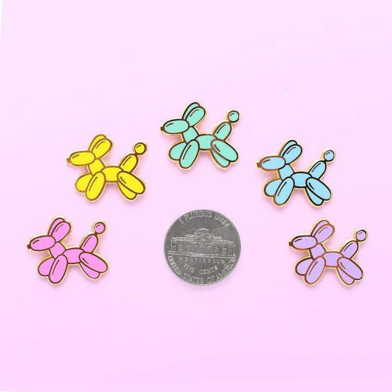 Six Balloon Dog Pins in different colors displayed around a quarter on a light pink background.