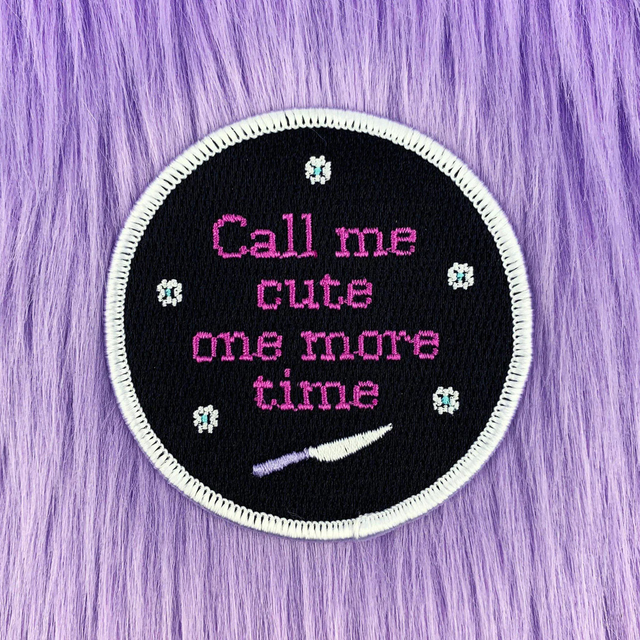 Round iron-on patch with “Call Me Cute,” flowers, a white knife, and a purple fur-like background.
