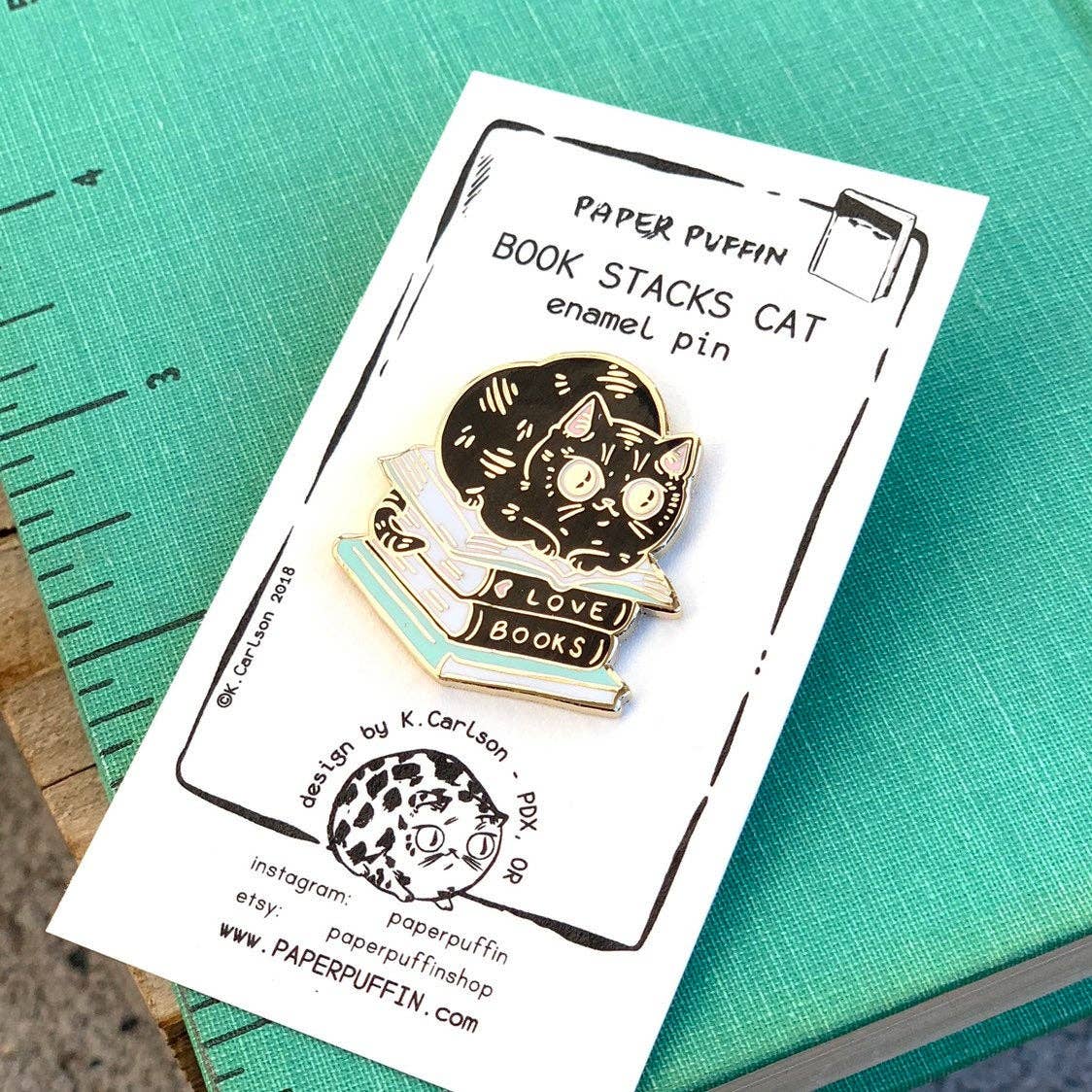 Black cat reading atop a stack of books labeled LOVE BOOKS enamel pin.