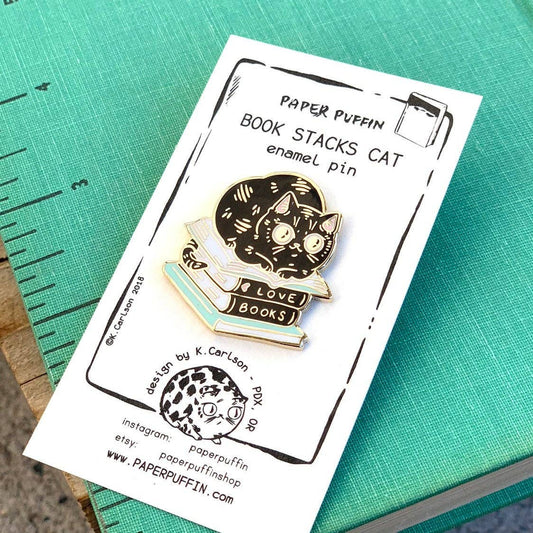 Black cat reading atop a stack of books labeled LOVE BOOKS enamel pin.
