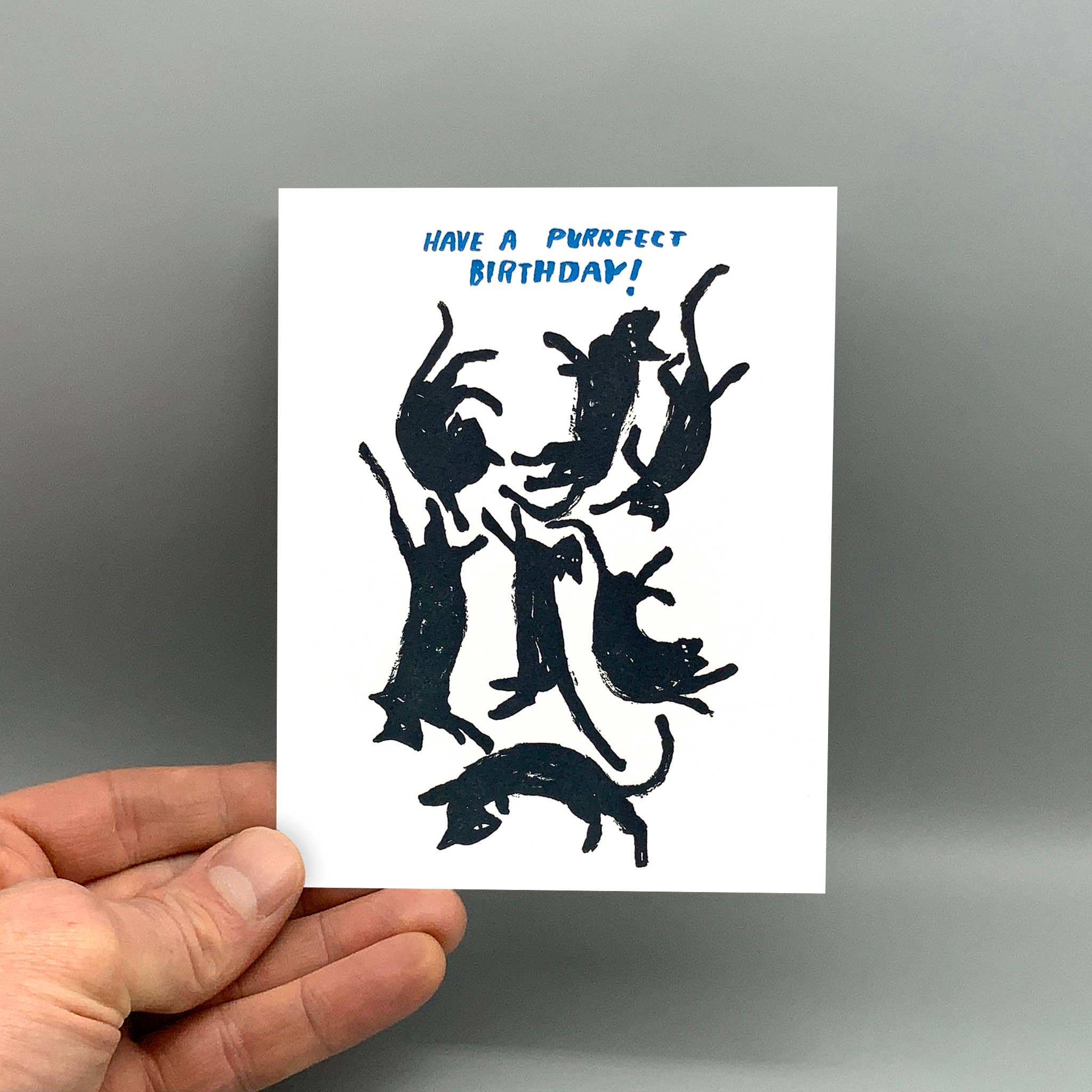 Purrfect Birthday greeting card with black cat silhouettes and festive text, held in a hand.