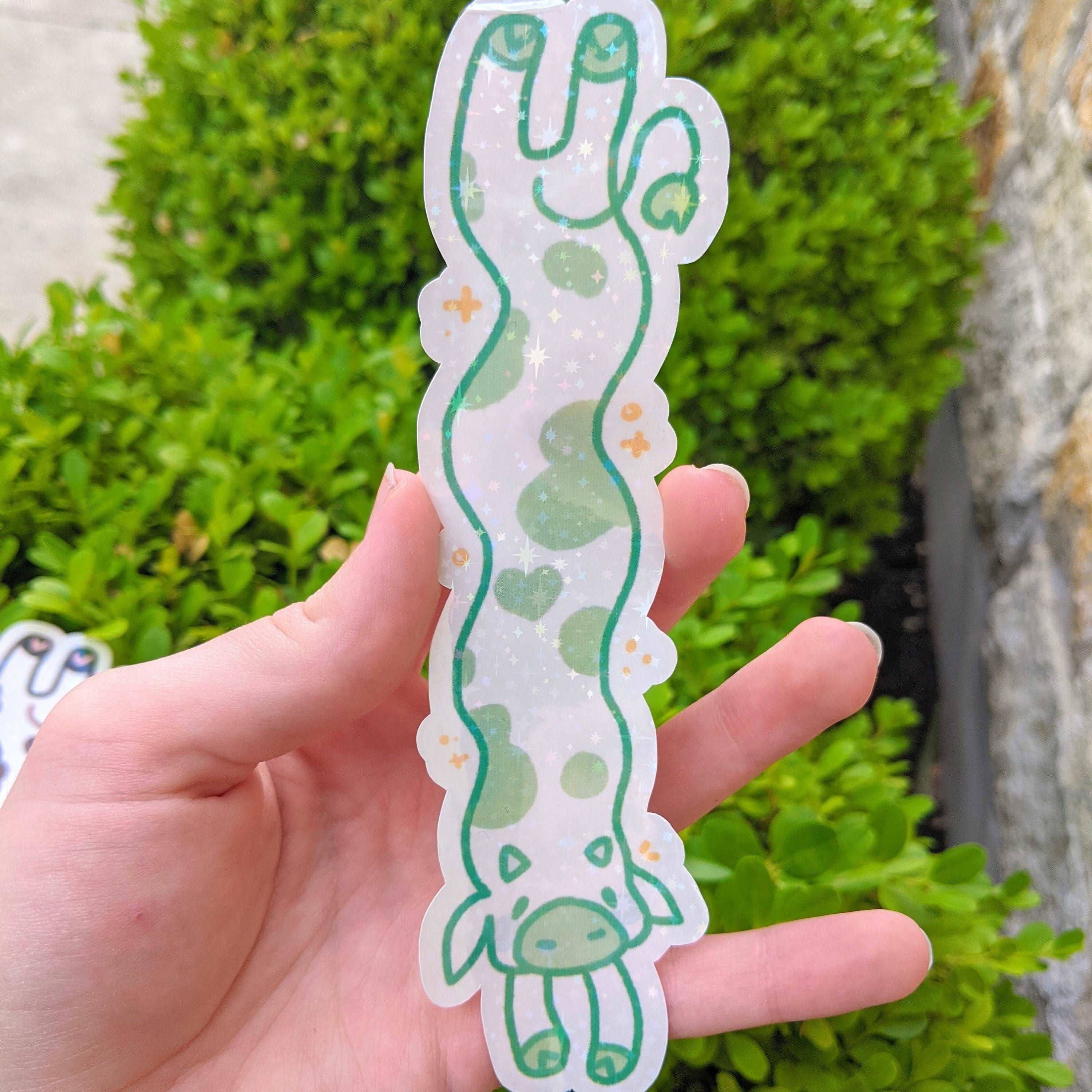 MORE Sparkly Long Cow Sticker with green spots held in a hand.