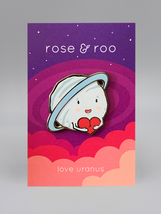 Love Uranus Enamel Pin showing a smiling Uranus with a heart, attached to a card labeled rose & roo.