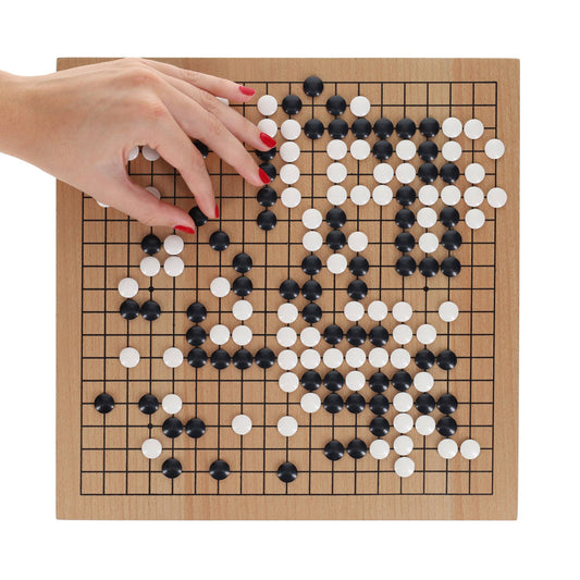 12 in. Wood GO Set board with scattered black and white stones; a hand places a white stone on the board.