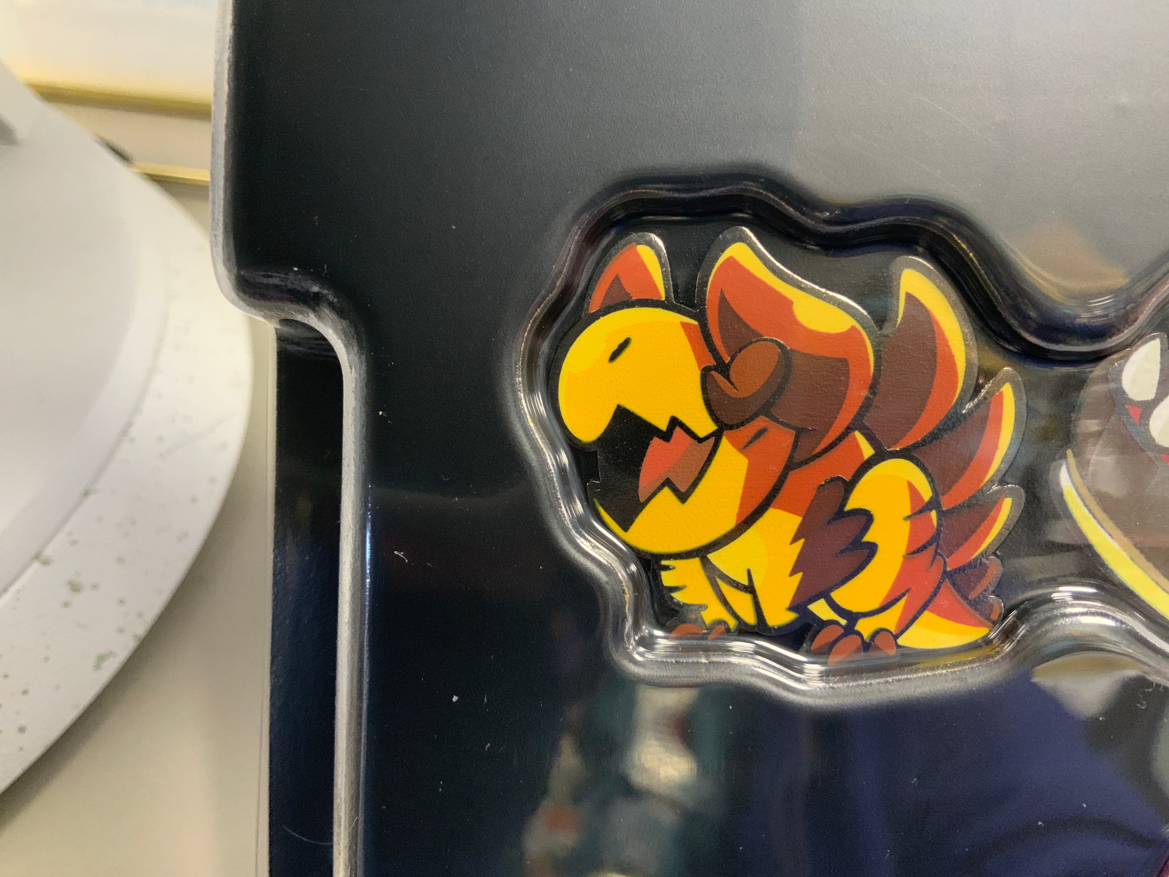 Heliana monster hunting pin Mechakobold featuring a yellow, orange, and brown cartoon creature on black packaging.