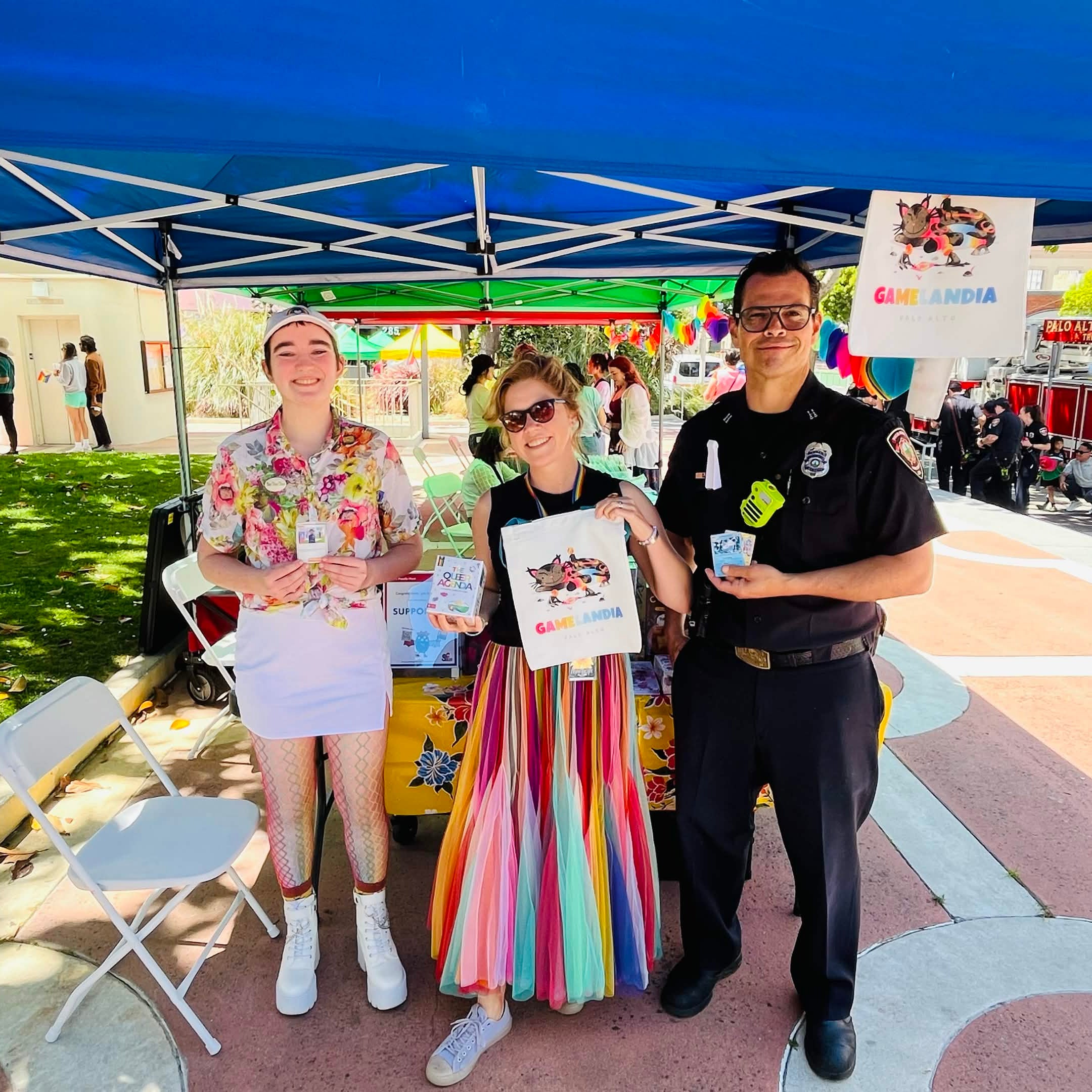 Two people and a police officer standing under a blue canopy at an outdoor event.