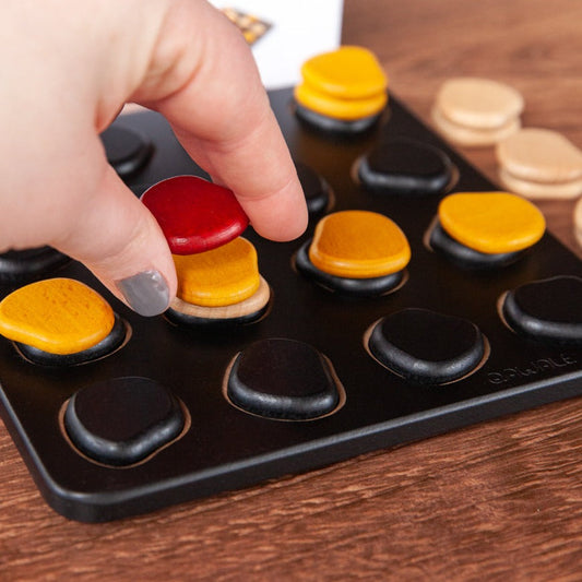 Qawale Mini board with yellow, beige, and red pieces; a hand places a red piece on the board.
