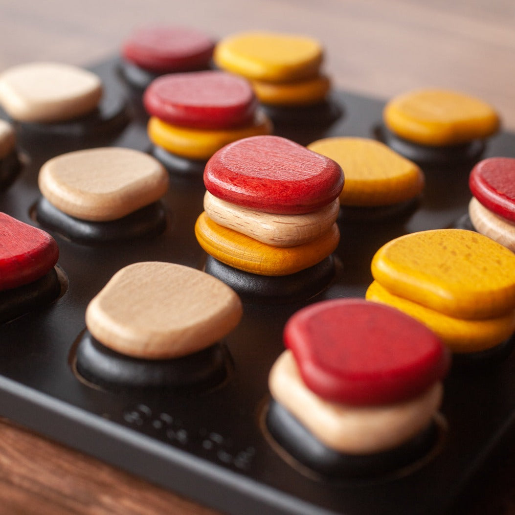 Qawale Mini wooden board game with stacked red, yellow, and beige pieces on a black grid.