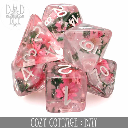 7-piece pink resin polyhedral dice set with flower inclusions, white numbers, labeled Cozy Cottage: Day.